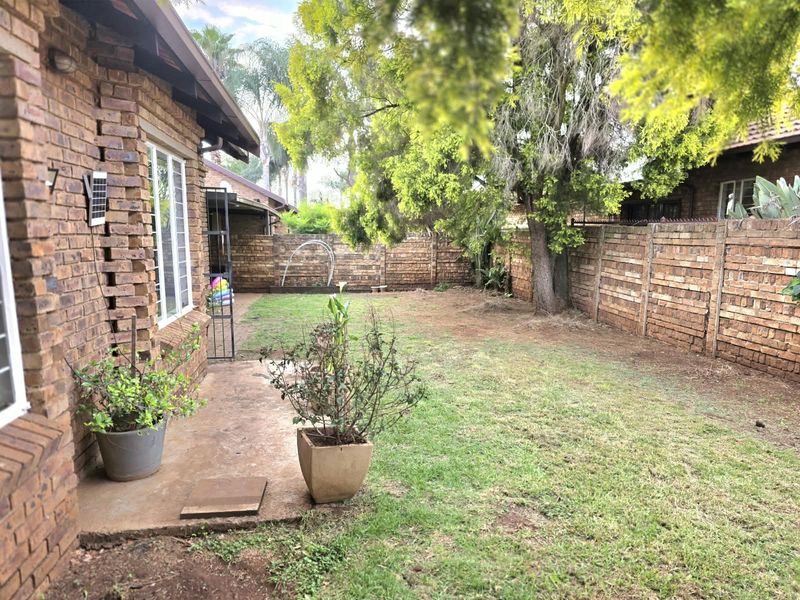 A private rear garden featuring a concrete patio area, established trees, and secure perimeter brick walling.