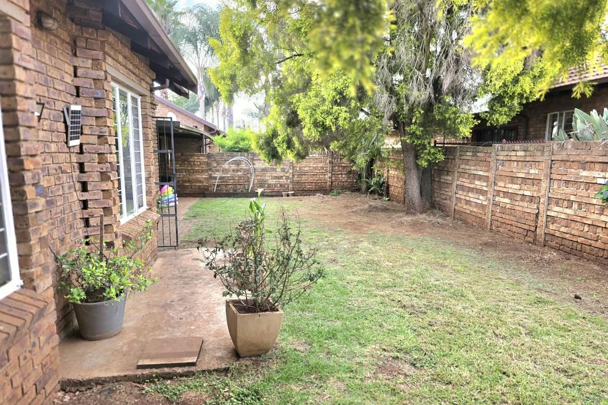 A private rear garden featuring a concrete patio area, established trees, and secure perimeter brick walling.