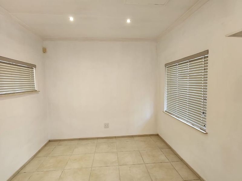 A bright, empty bedroom featuring neutral tiled flooring, recessed downlighting, and fitted venetian blinds, offering a clean canvas for personalization.