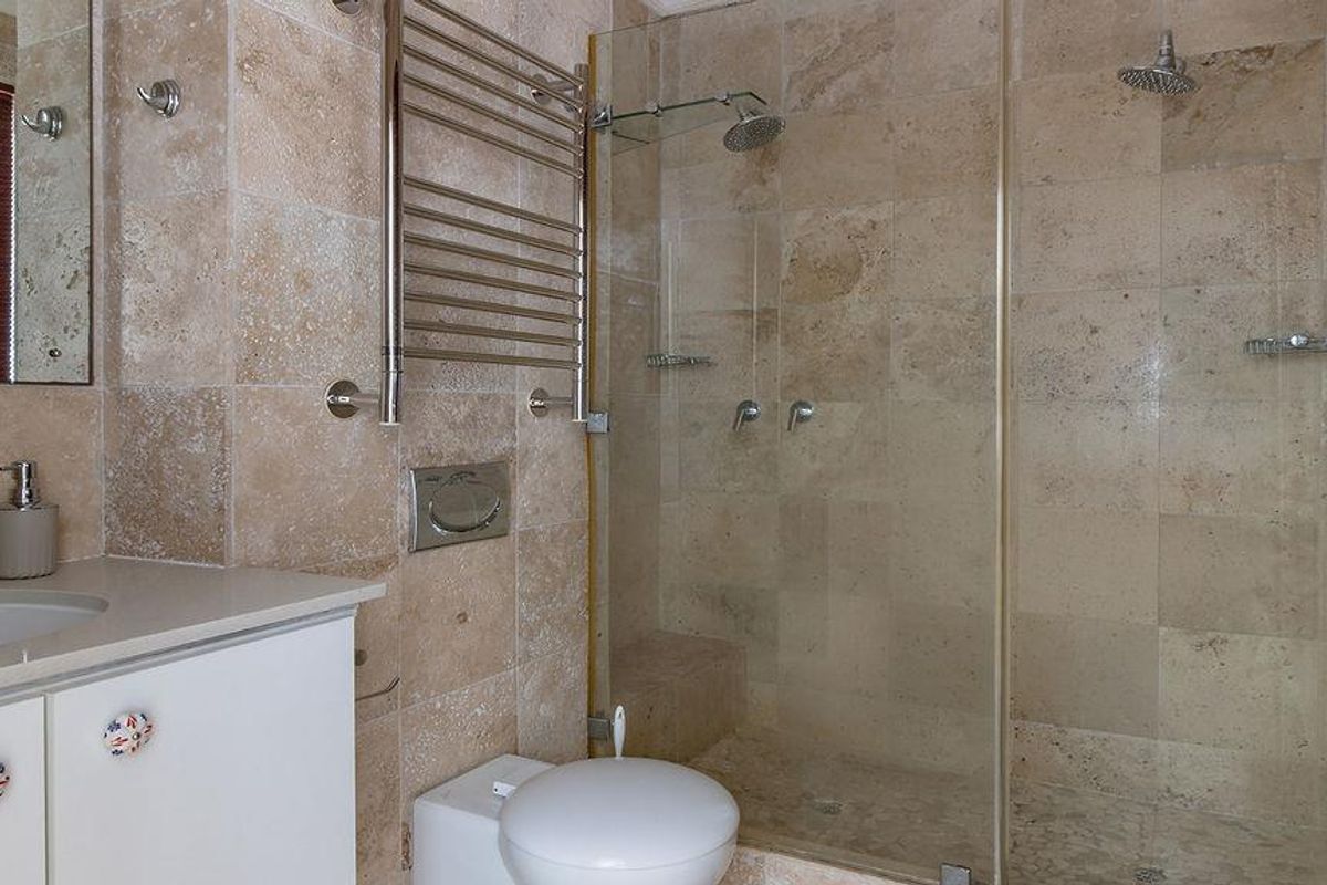 Modern bathroom featuring travertine wall and floor tiles, a spacious walk-in shower with dual shower heads, and a wall-mounted vanity with integrated sink.