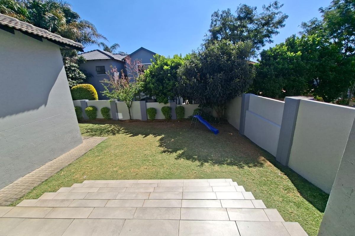 A well-maintained rear garden featuring a tiled patio area, manicured lawn, and secure boundary walls.