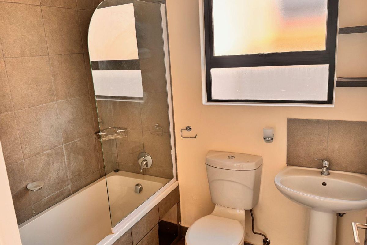 A functional bathroom featuring a bathtub with a glass screen, pedestal sink, and toilet, finished with neutral wall tiles.