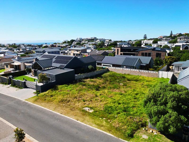 Aerial view of a vacant residential plot situated in a developed neighborhood with established boundary walls and street access.