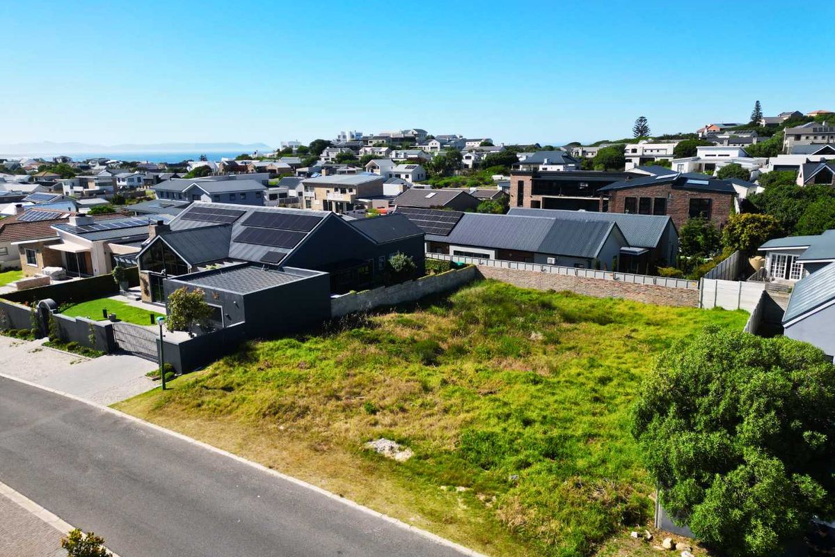 Aerial view of a vacant residential plot situated in a developed neighborhood with established boundary walls and street access.