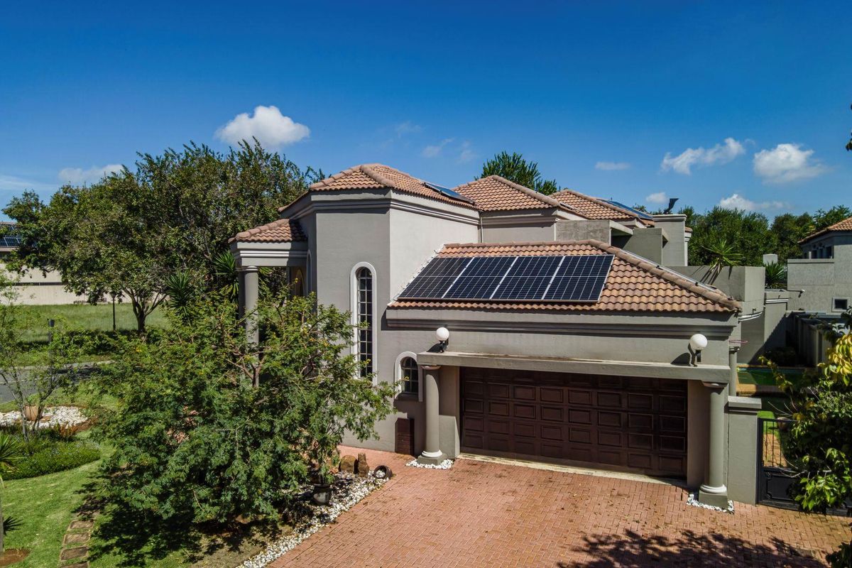 Aerial view of a residential property featuring a tiled roof, solar panels, and a paved driveway leading to a garage.