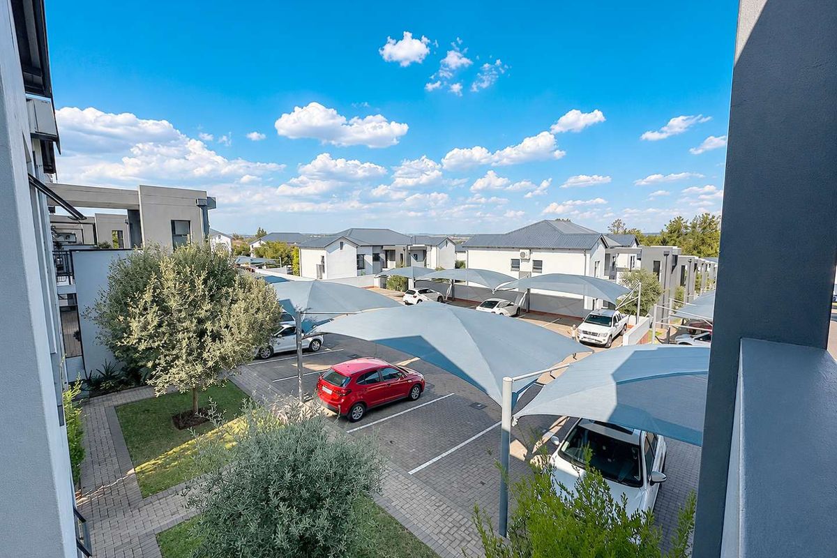 Elevated view of the apartment complex parking area featuring paved bays, shade cloth carports, and well-maintained landscaped garden spaces.