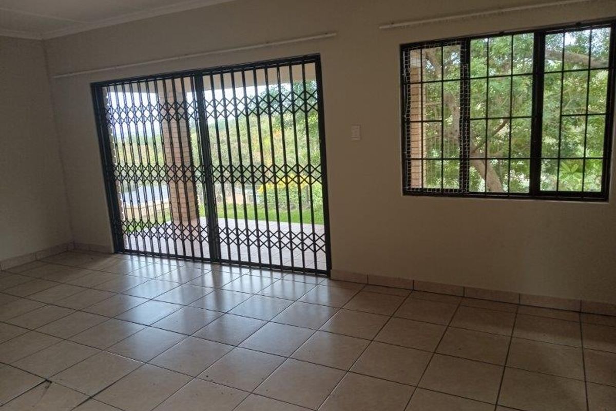 An empty living room featuring ceramic floor tiles, a sliding security gate, and window security bars, offering a bright and functional space.
