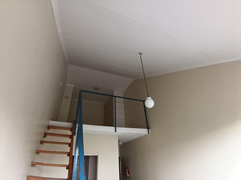An open-plan living area featuring a mezzanine level accessed by a timber staircase with a metal balustrade and a high ceiling.