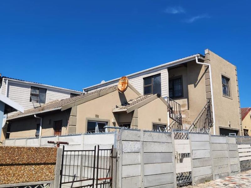 Front exterior view of a multi-story residential property featuring a precast concrete boundary wall, metal security gate, and external staircase access.