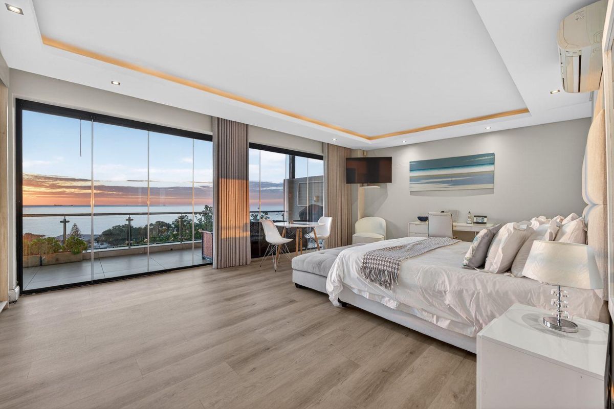 Spacious master bedroom featuring modern laminate flooring, recessed cove lighting, and large sliding glass doors opening to a private balcony with ocean views.