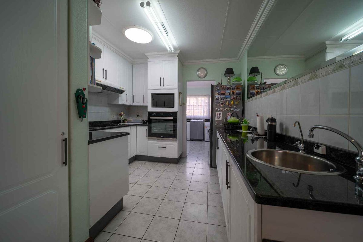A functional kitchen featuring white cabinetry, dark granite countertops, a built-in oven, and a stainless steel sink, with an adjacent laundry area visible.