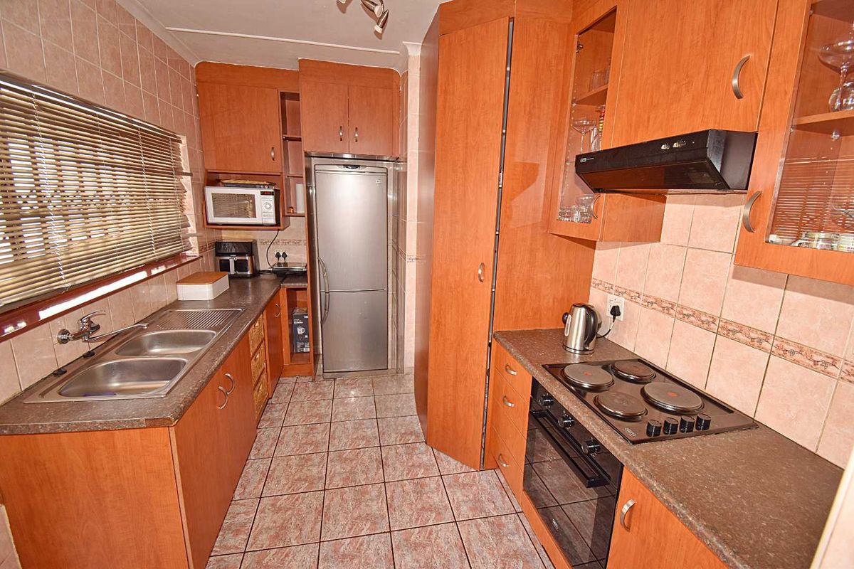 A functional kitchen featuring wood-look cabinetry, tiled splashbacks, a double sink, and built-in cooking appliances including an oven and electric hob.