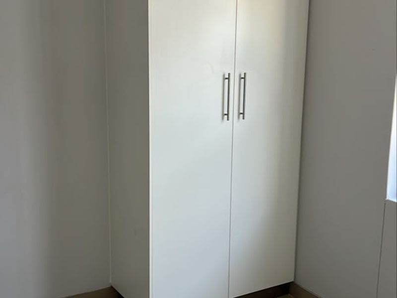 A clean, empty bedroom featuring neutral tiled flooring and a modern white built-in wardrobe with sleek metal handles.