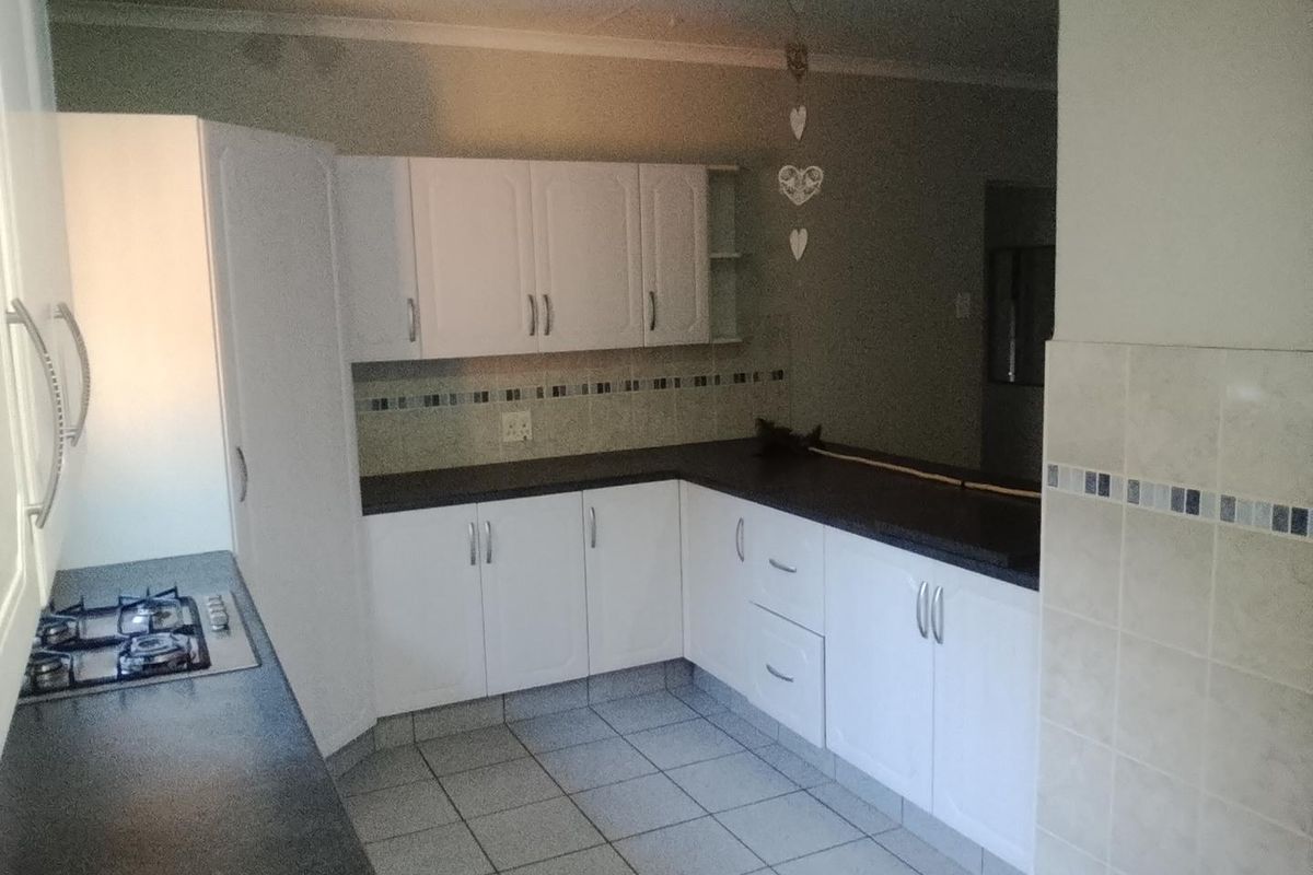 A functional kitchen featuring white built-in cabinetry, dark laminate countertops, a gas hob, and tiled flooring with a tiled backsplash.