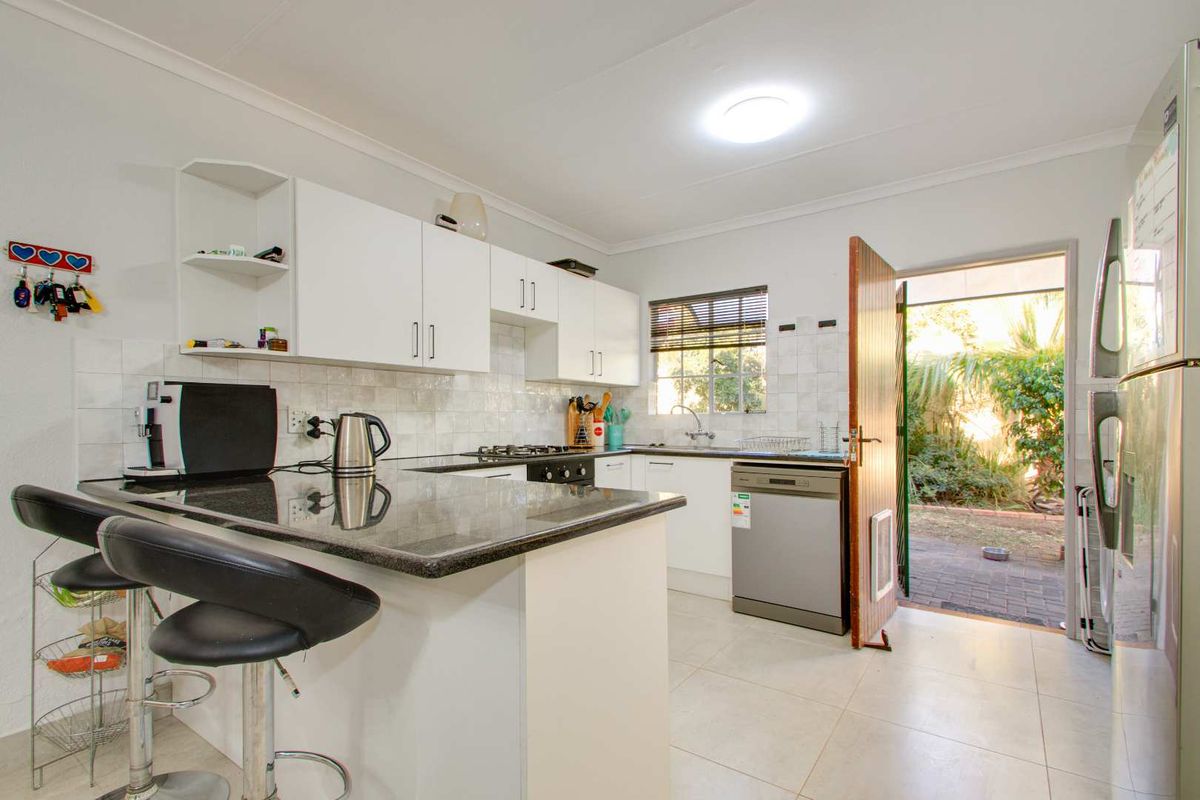 Functional kitchen featuring granite countertops, white cabinetry, built-in gas hob, and direct access to the rear garden area.