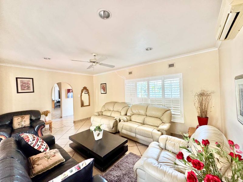 Spacious living room featuring tiled flooring, plantation shutters, recessed lighting, and a ceiling fan, with an arched entryway leading to adjacent areas.
