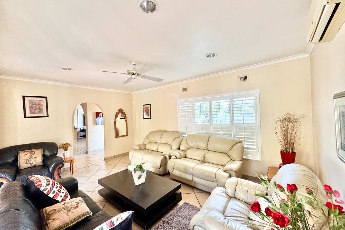 Spacious living room featuring tiled flooring, plantation shutters, recessed lighting, and a ceiling fan, with an arched entryway leading to adjacent areas.