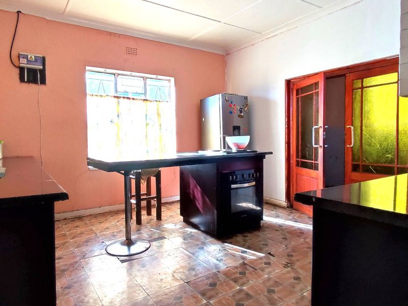 A dated kitchen featuring a central island with a built-in oven, tiled flooring, and timber door access, offering potential for modernization.