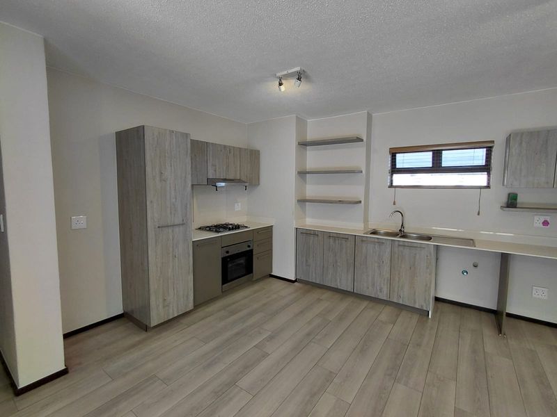 Modern kitchen featuring light wood-grain cabinetry, stone countertops, gas hob, electric oven, and integrated sink with ample storage and floating shelving.