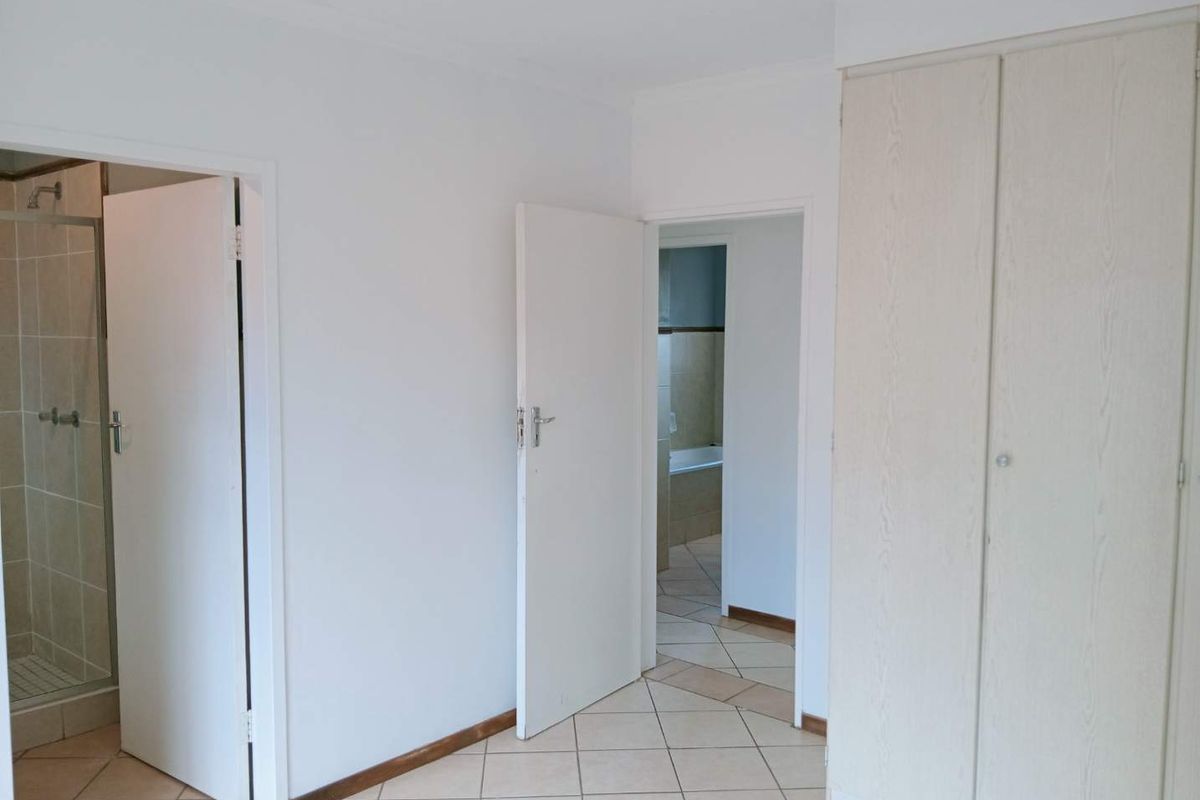 A bedroom interior featuring built-in cupboards, tiled flooring, and direct access to an en-suite bathroom with a shower.