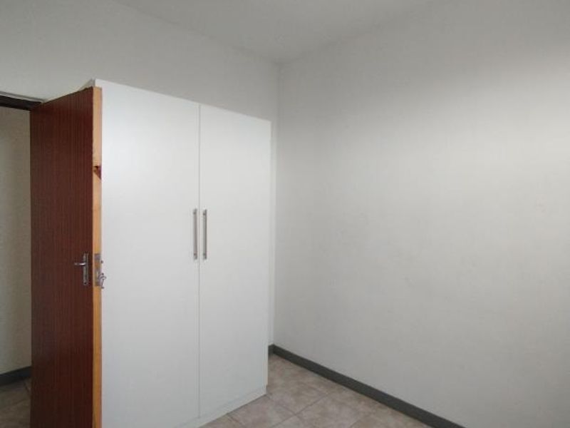 A simple bedroom featuring tiled flooring and a built-in white wardrobe.
