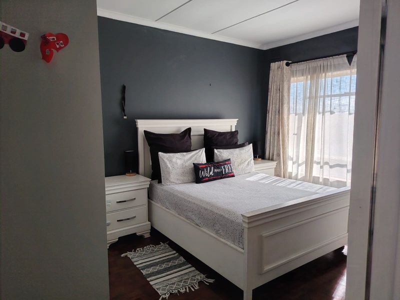A well-lit bedroom featuring dark accent walls, laminate flooring, and large windows with curtains, providing a comfortable and modern living space.