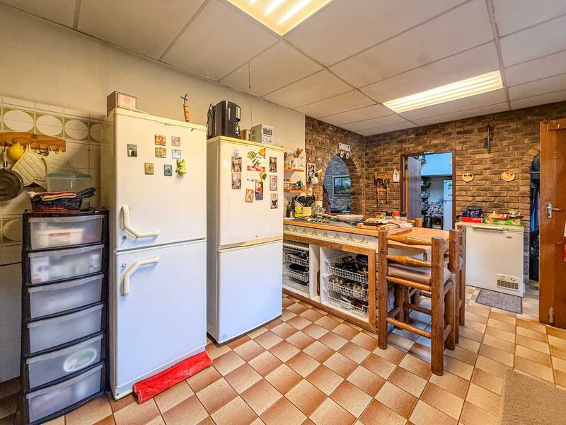 A rustic kitchen featuring exposed brick walls, tiled flooring, and a central island with built-in storage, offering a dated but functional layout.