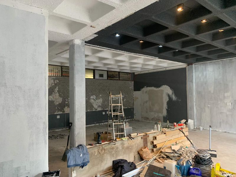 Open-plan retail space currently undergoing renovation, featuring a distinctive waffle slab ceiling, recessed lighting, and exposed structural elements ready for final finishes.