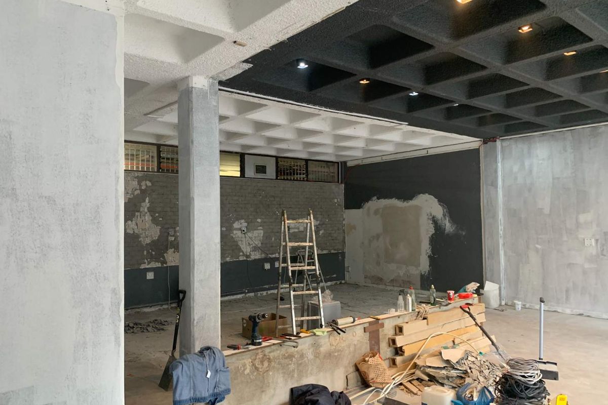 Open-plan retail space currently undergoing renovation, featuring a distinctive waffle slab ceiling, recessed lighting, and exposed structural elements ready for final finishes.