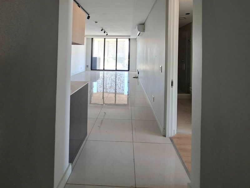 Spacious open-plan living area featuring polished floor tiles, modern track lighting, and large sliding doors leading to a balcony.