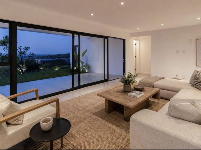 Modern living room featuring large sliding glass doors that open to an outdoor patio, recessed lighting, and neutral tiled flooring.