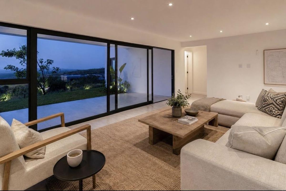 Modern living room featuring large sliding glass doors that open to an outdoor patio, recessed lighting, and neutral tiled flooring.