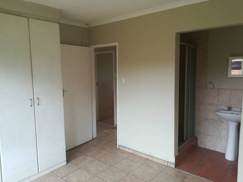 A vacant bedroom featuring built-in cupboards, tiled flooring, and an attached en-suite bathroom with a pedestal basin and shower cubicle.