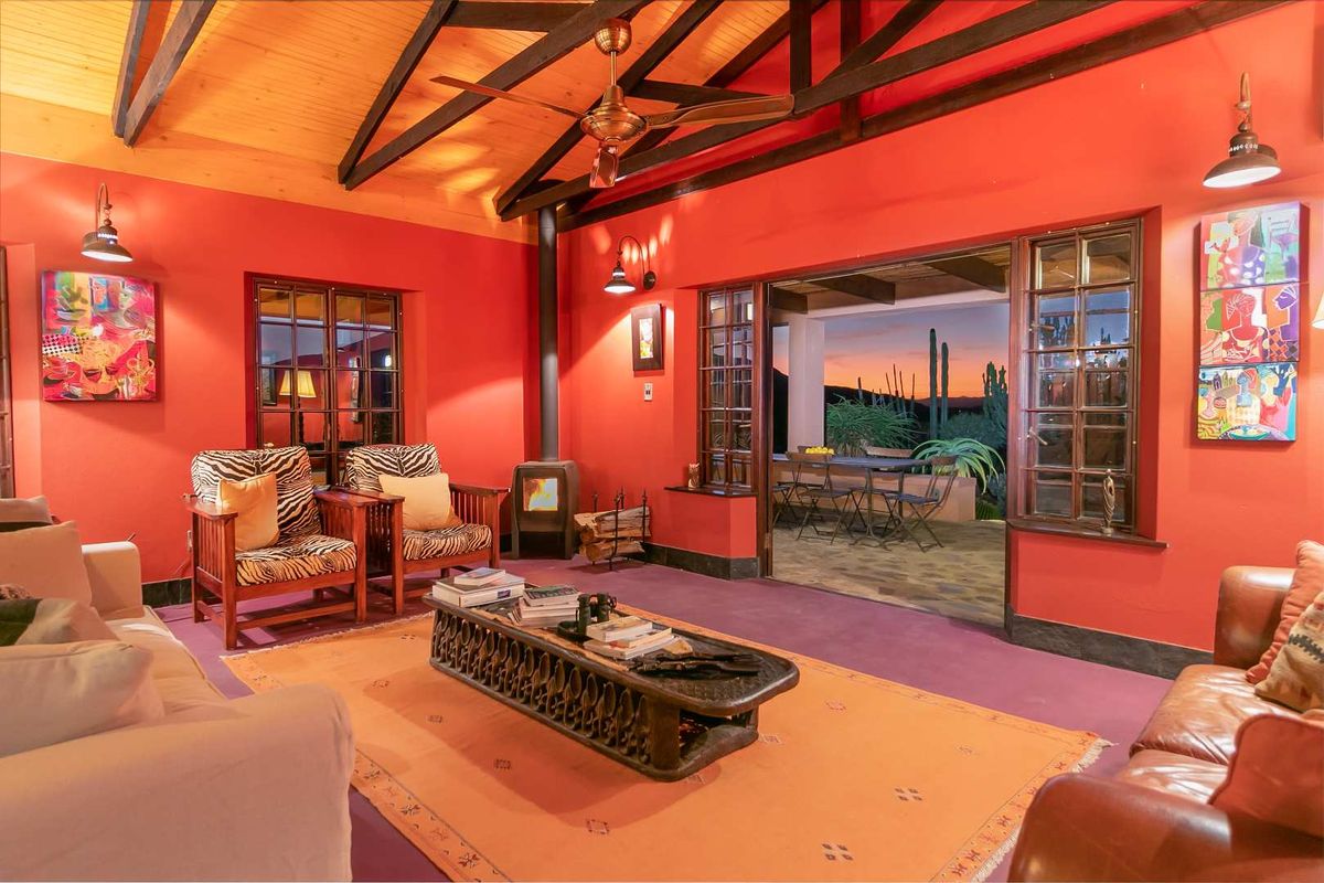 Spacious living room featuring exposed timber beams, a wood-burning fireplace, and large glass doors opening onto a covered patio with scenic landscape views.