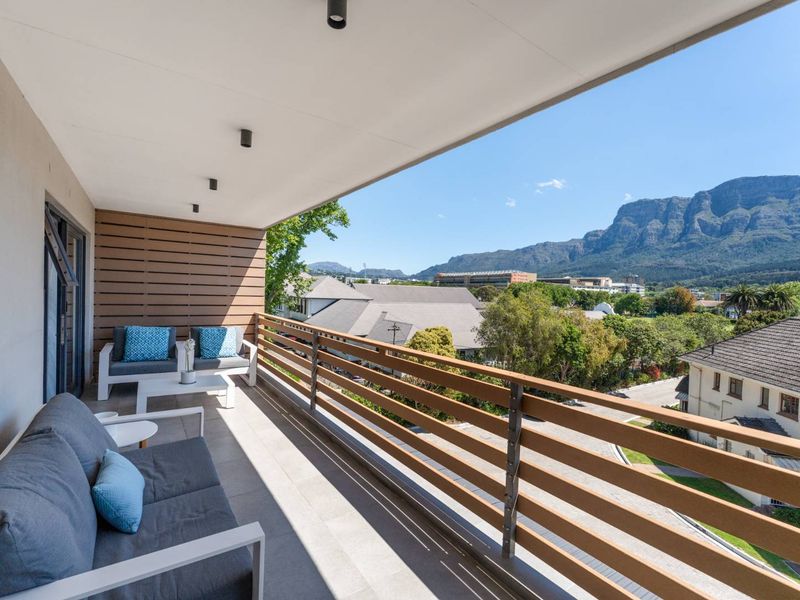 Spacious covered balcony featuring modern tiled flooring, timber-look privacy screening, and a sleek balustrade, offering expansive mountain and neighbourhood views.