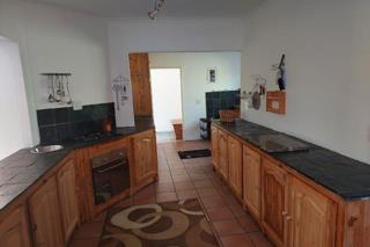 A functional kitchen featuring wooden cabinetry, stone countertops, built-in oven, and hob, with tiled flooring throughout.