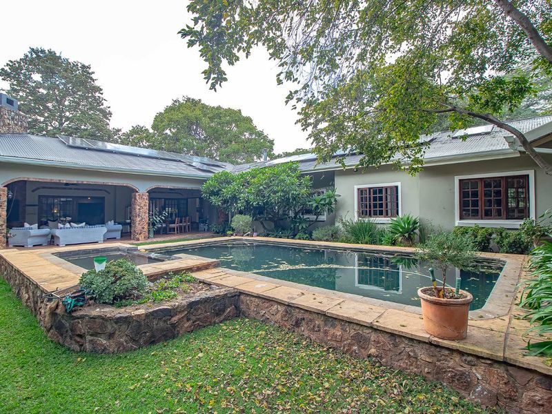 Spacious rear garden featuring a swimming pool with stone surround, covered patio area, and solar panels installed on the pitched roof.