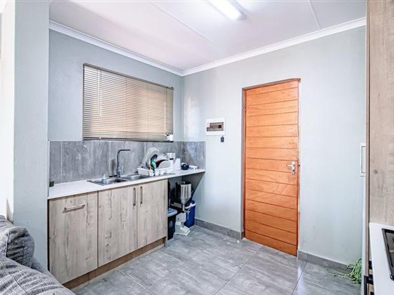 A functional laundry area featuring built-in cabinetry, a stainless steel sink, tiled splashback, and durable tiled flooring with a wooden door.