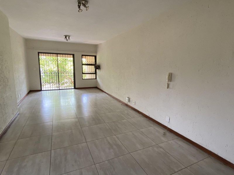 An empty, open-plan living area featuring tiled flooring, a sliding door with security gate, and an intercom system.