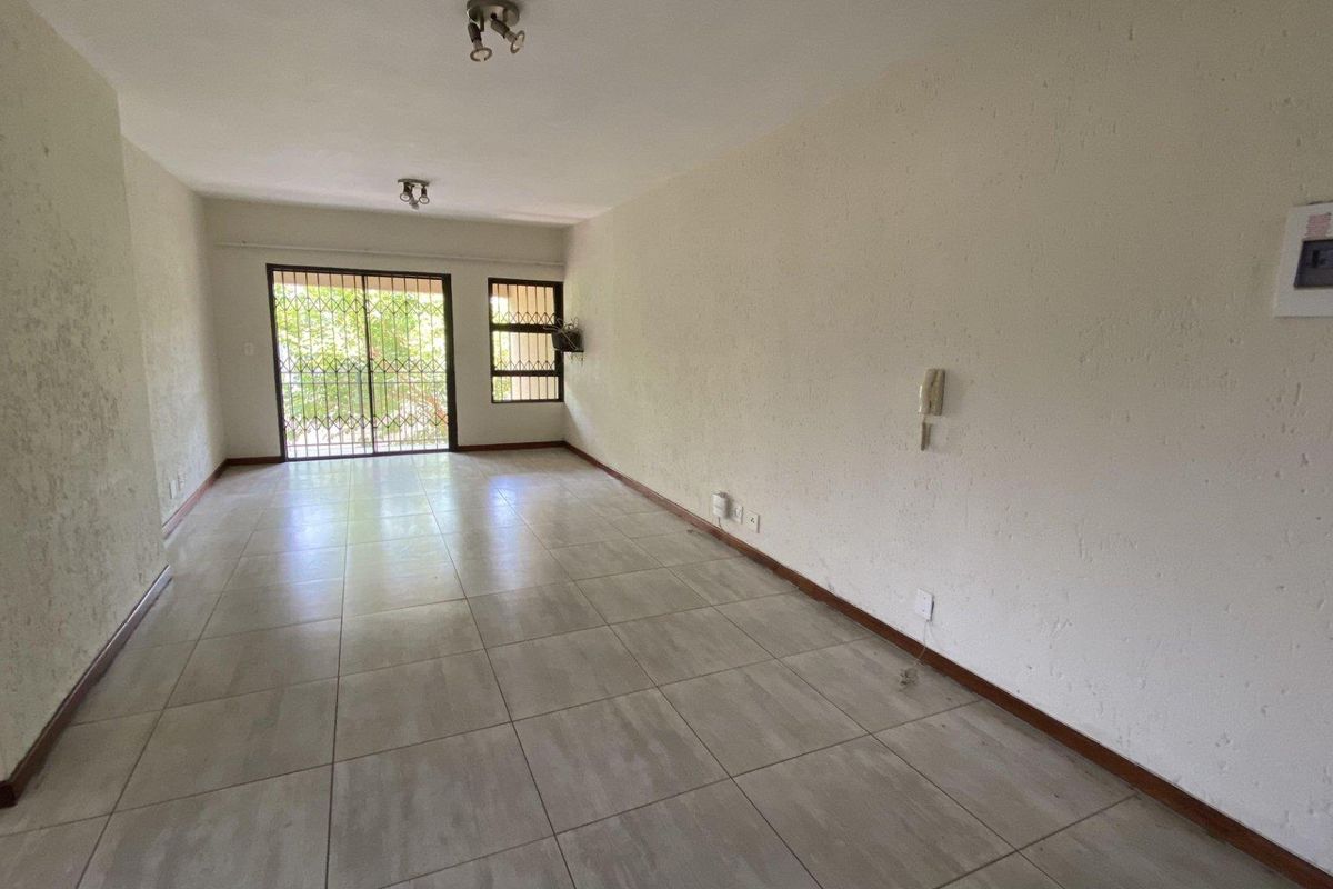 An empty, open-plan living area featuring tiled flooring, a sliding door with security gate, and an intercom system.