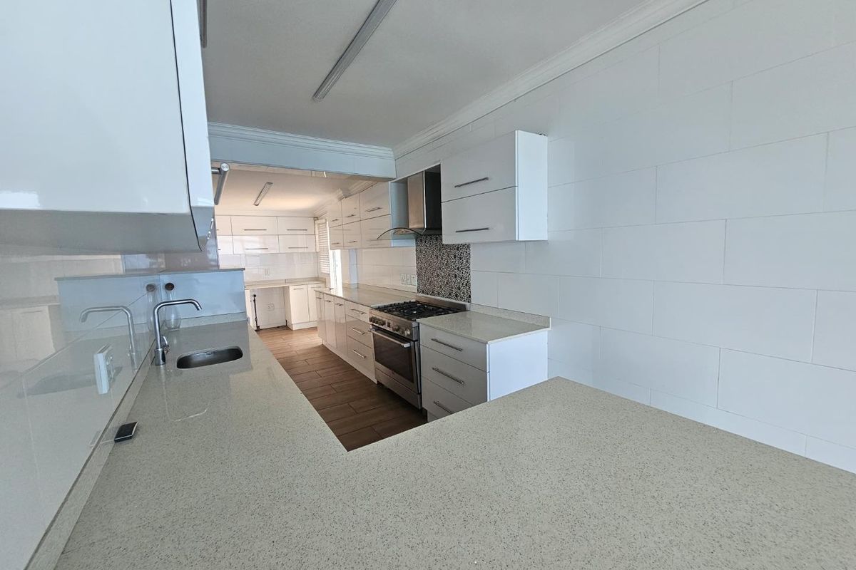 Modern kitchen featuring white cabinetry, stone countertops, stainless steel gas stove, extractor fan, and tiled flooring in a clean, open layout.