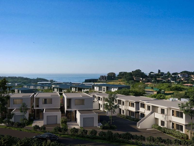 An aerial view of a modern townhouse development featuring multiple units, paved driveways, and garages, set within a coastal landscape.