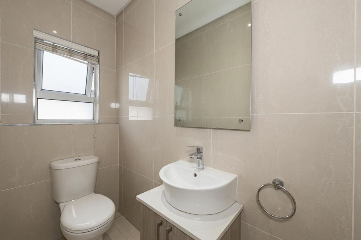 Modern bathroom featuring floor-to-ceiling neutral tiling, a contemporary vanity with a vessel sink, a wall-mounted mirror, and a toilet.
