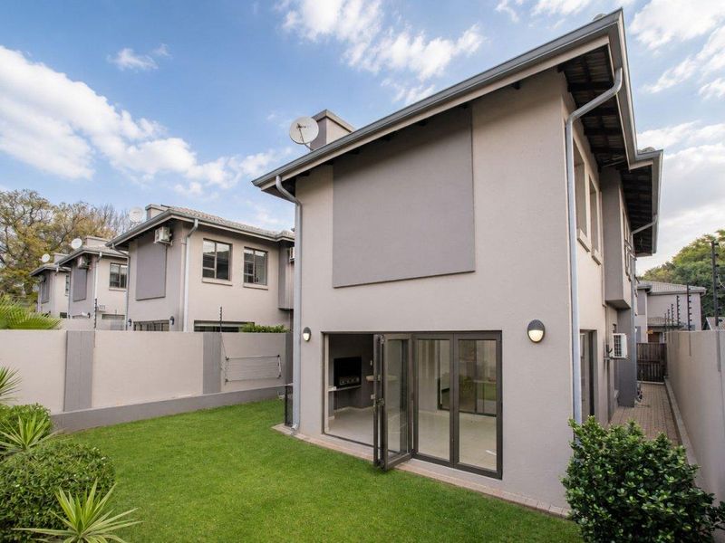 Rear view of a modern townhouse featuring a private garden, bi-fold doors leading to the interior, and well-maintained exterior finishes.
