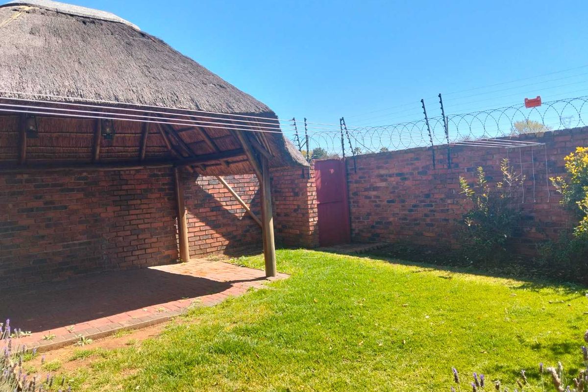 A private rear garden featuring a thatched lapa, paved patio area, and secure brick boundary walls topped with electric fencing.
