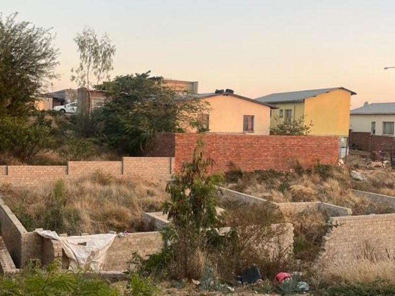 A vacant residential plot featuring unfinished brick foundation walls and boundary fencing, situated in a developed neighborhood setting.