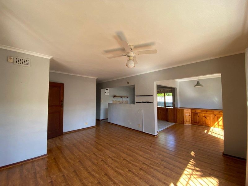 Spacious open-plan living and dining area featuring laminate flooring, a ceiling fan, and built-in wooden cabinetry in the adjacent kitchen space.