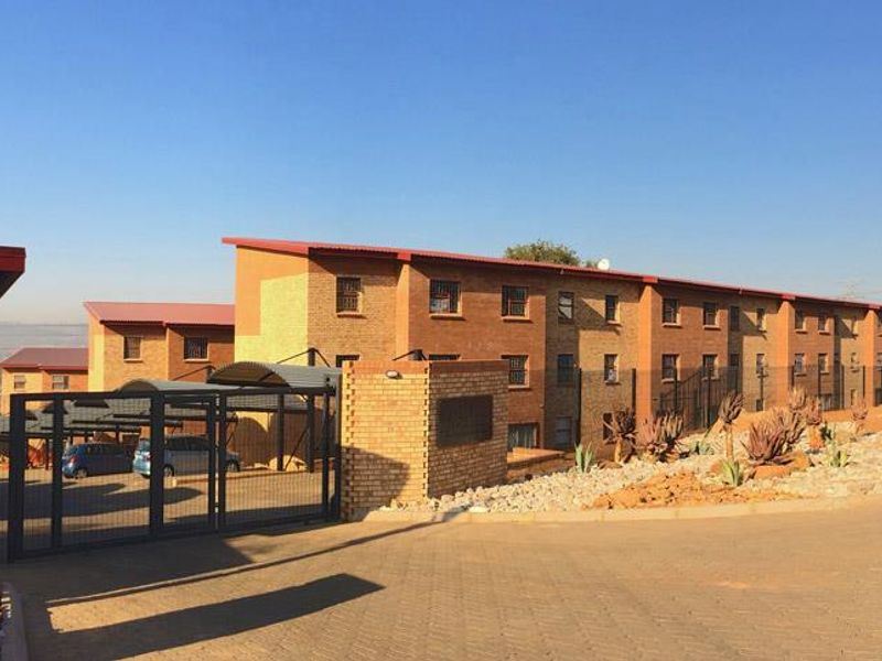 Exterior view of a multi-story brick apartment complex featuring a secure gated entrance, paved driveway, and covered carport parking facilities.