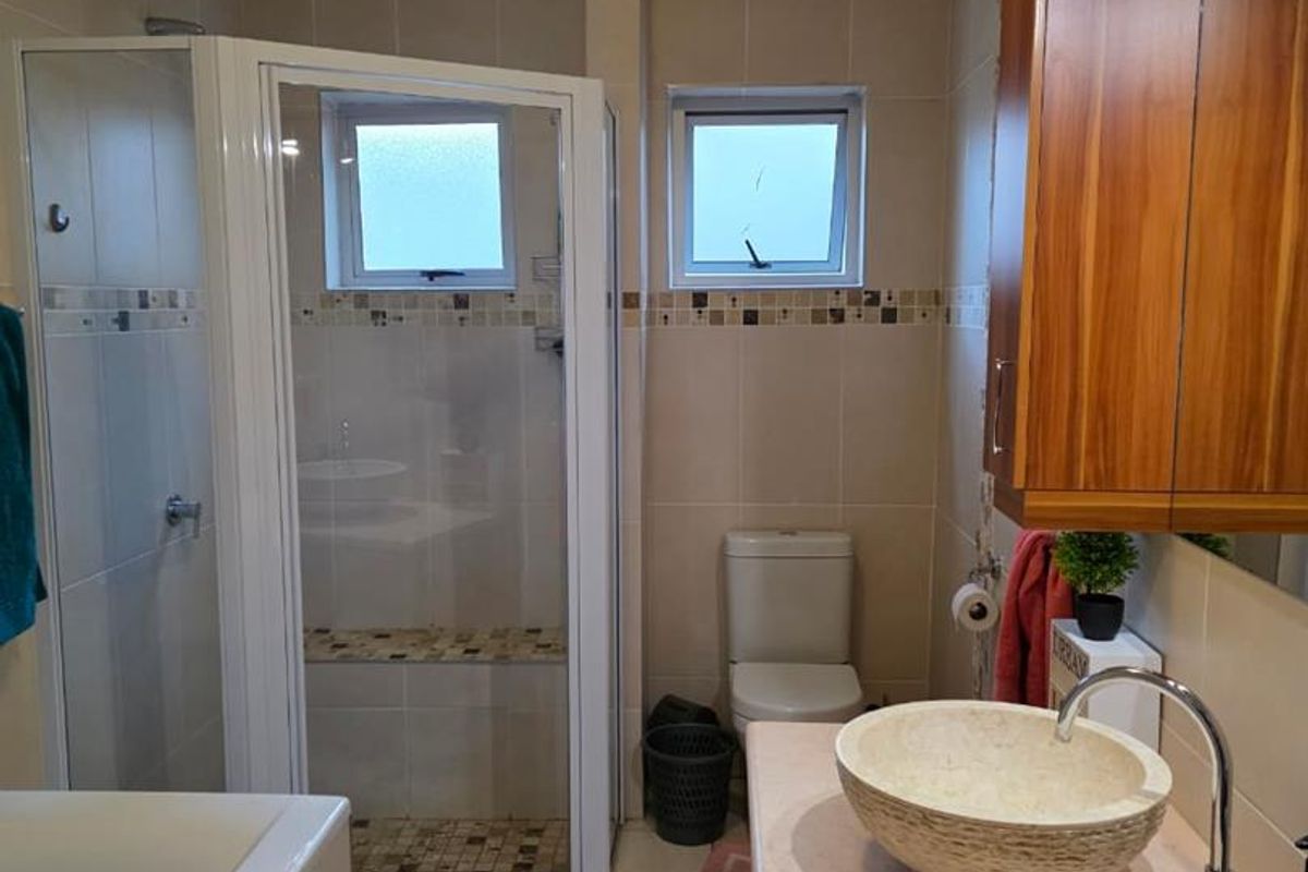 A well-maintained bathroom featuring a corner shower enclosure, a vessel sink on a vanity, a bathtub, and neutral wall tiling.