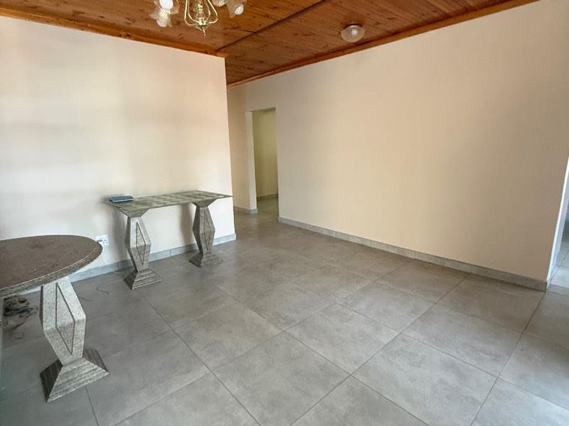 An open-plan living area featuring large format ceramic floor tiles and a traditional timber tongue and groove ceiling.